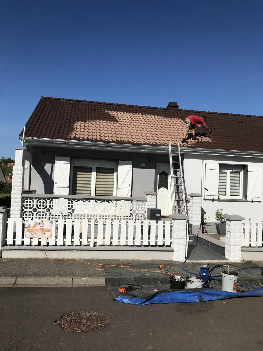 Couvreur au travail sur un toit en tuiles, bâche prête au pied de la maison