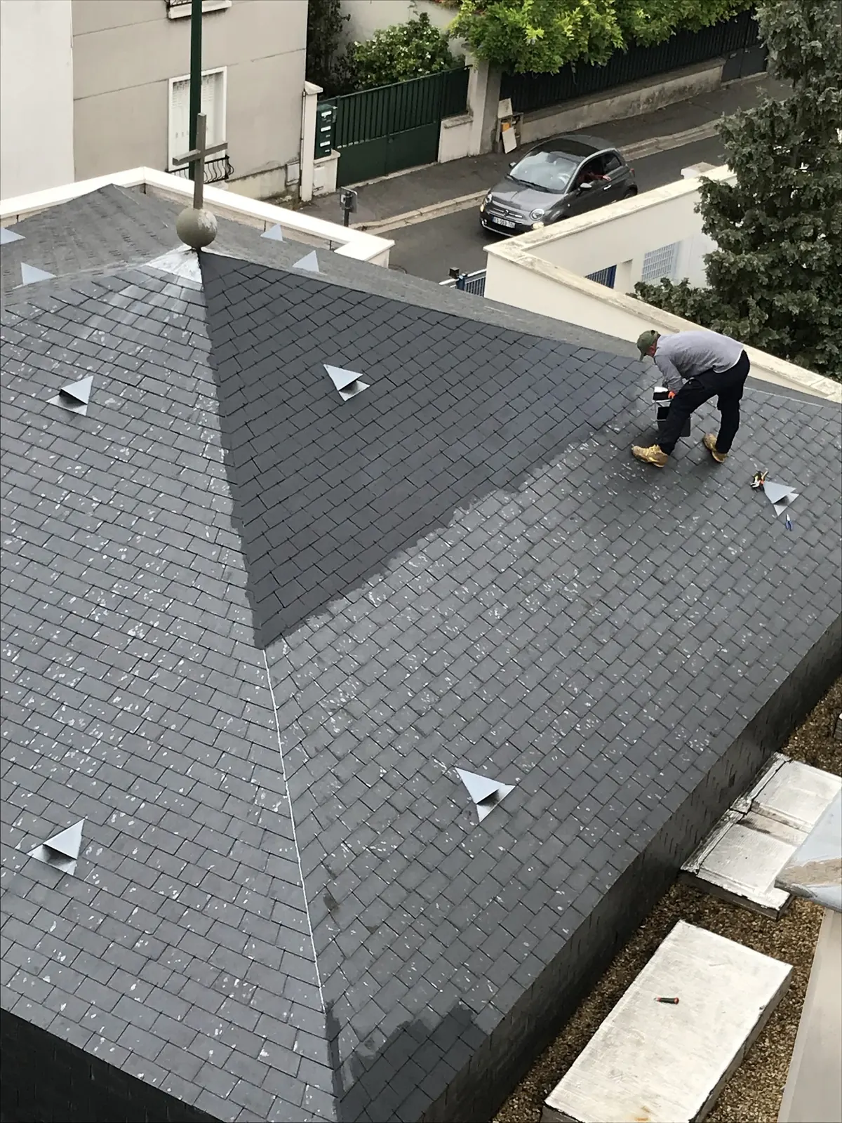 Couvreur au travail sur une toiture en ardoise à quatre pans, vue d’en haut