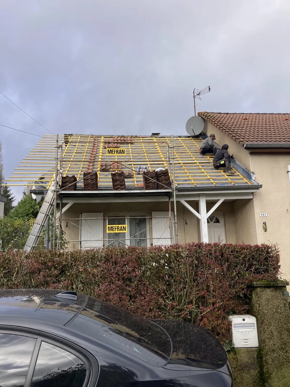 Deux couvreurs sur une toiture ouverte jusqu’aux liteaux, tuiles empilées, échafaudage en façade