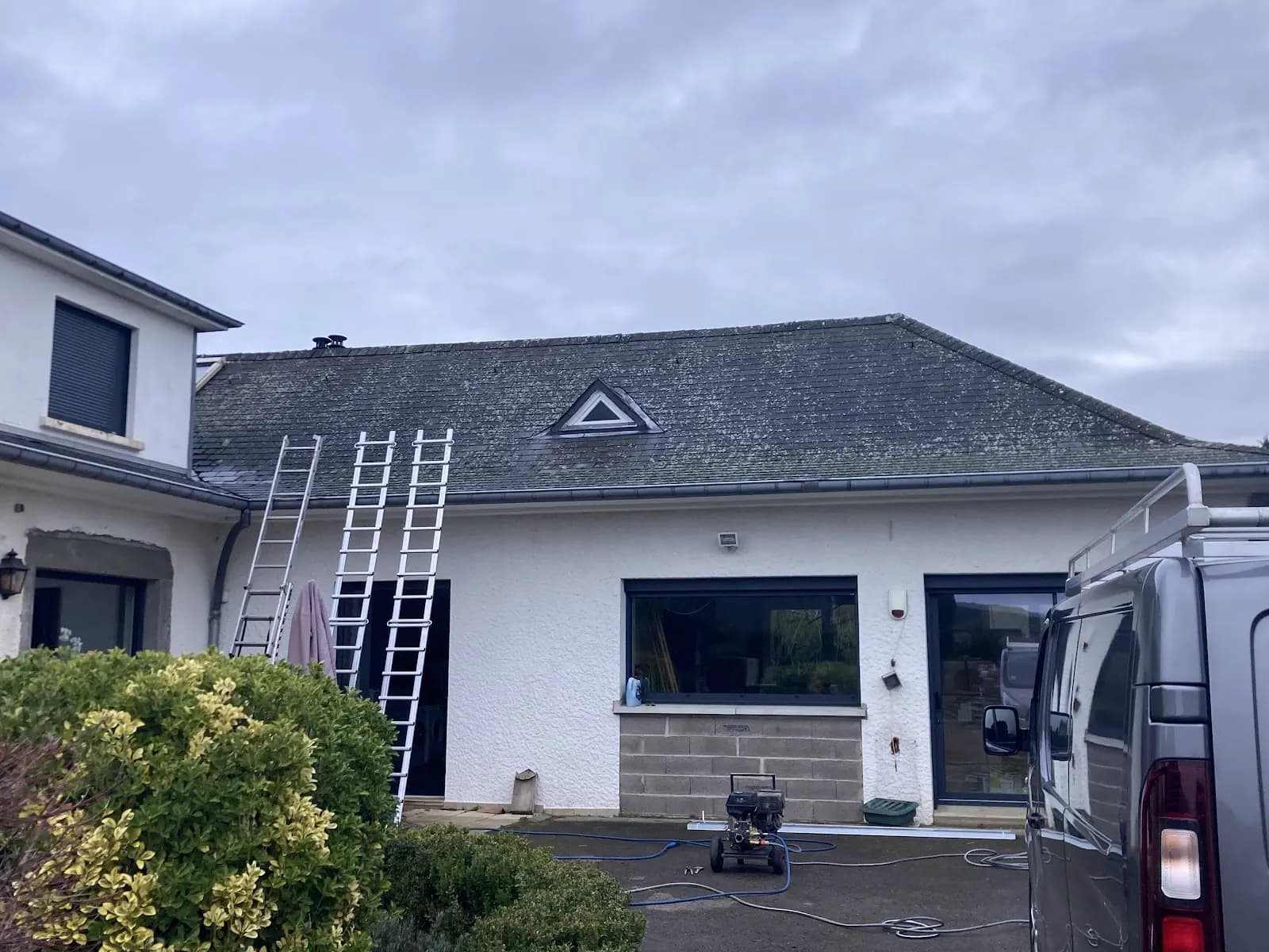 Maison à toiture en ardoise, trois échelles et un nettoyeur haute pression au pied de la façade