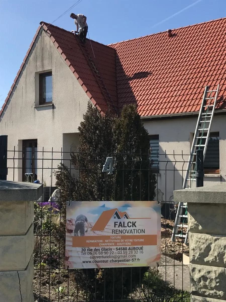 Panneau de chantier Falck Rénovation devant une maison, couvreur sur le toit