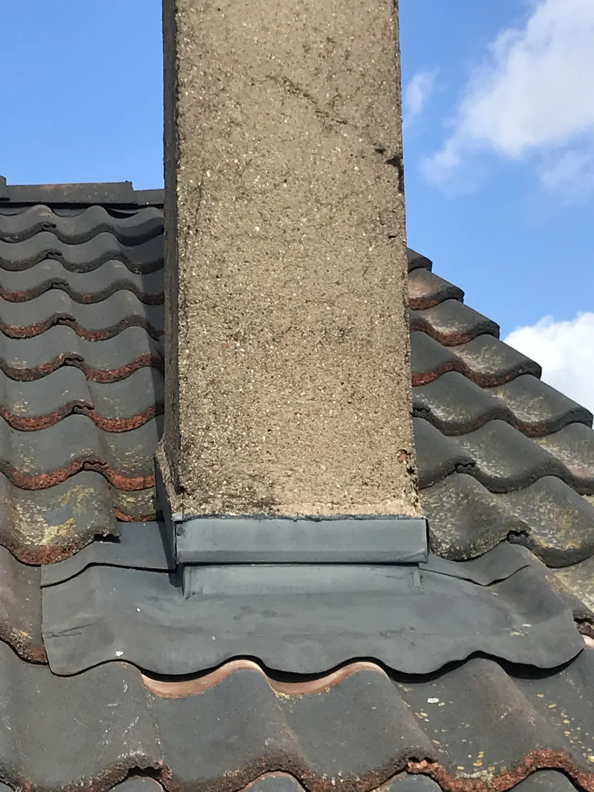 Souche de cheminée avec son solin sur une toiture en tuiles sombres